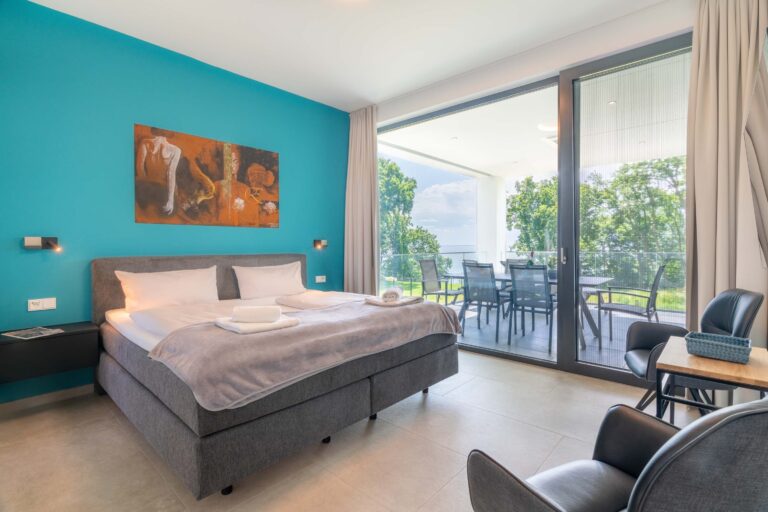 Schlafzimmer der Ferienwohnung mit Boxspringbett und Balkonblick ins Grüne